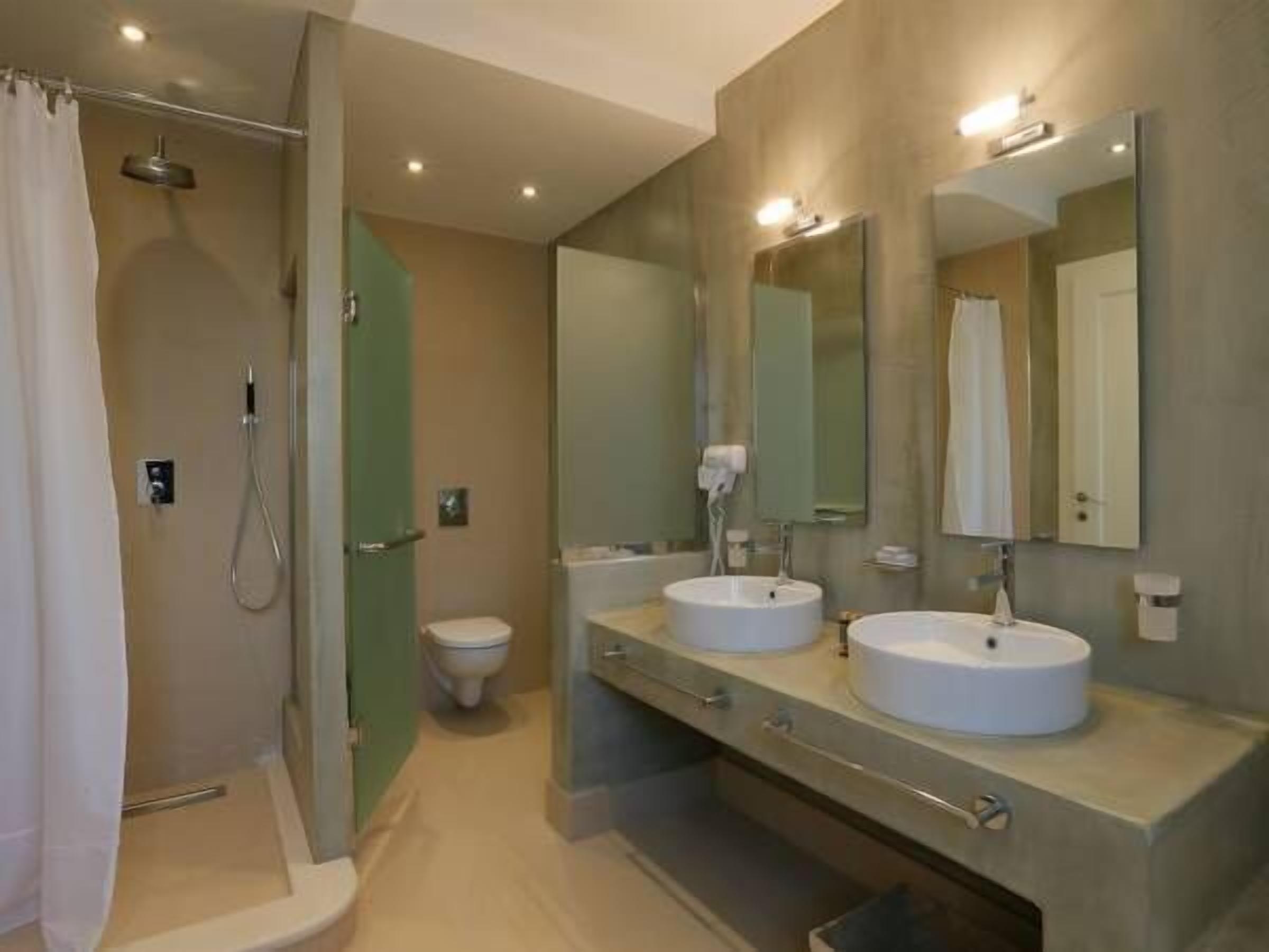A modern bathroom with a walk-in shower, a toilet, and a vanity with two sinks and a large mirror.