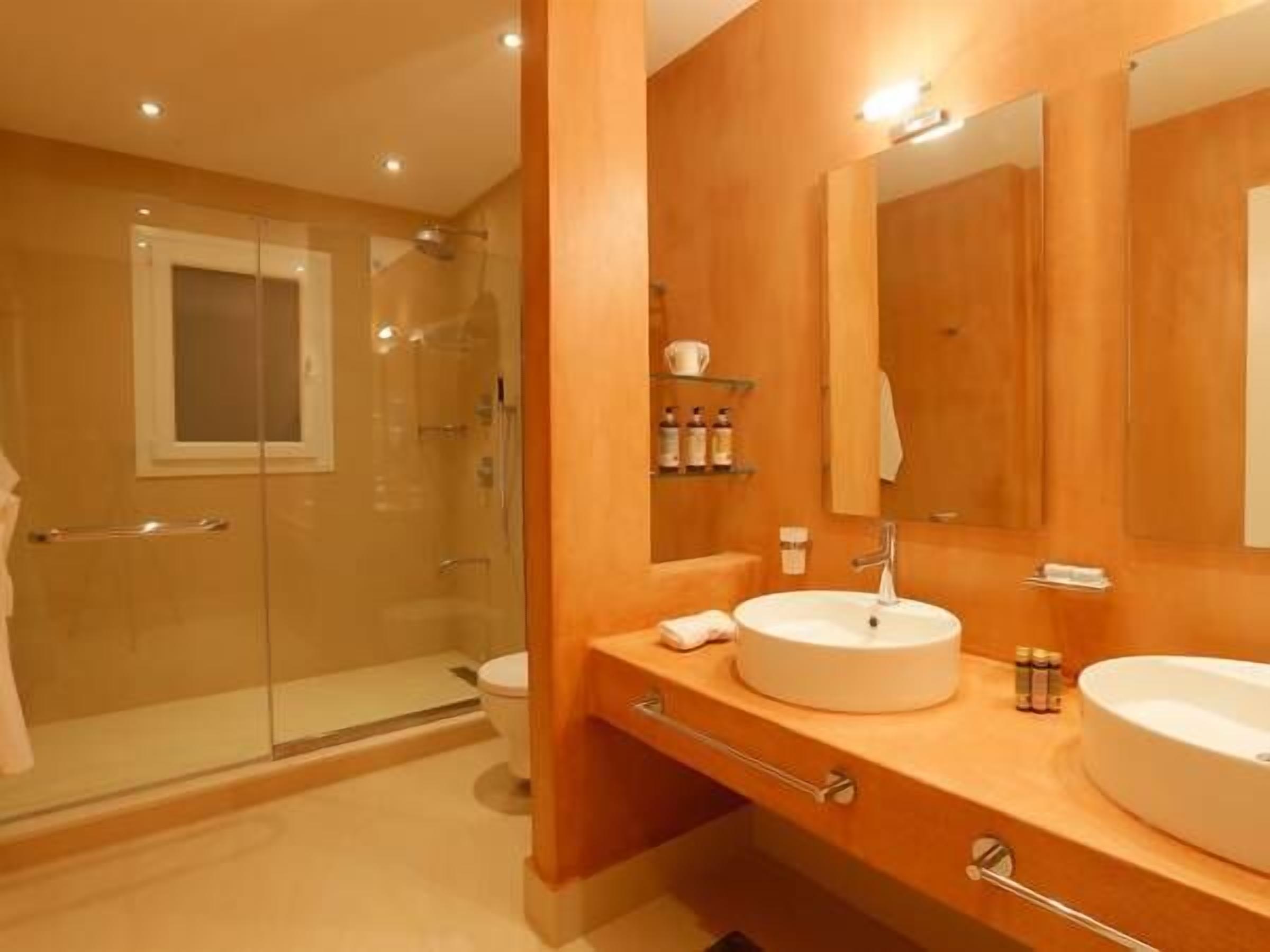 A modern bathroom with a glass shower enclosure, a large mirror, two sinks, and a vanity with storage.