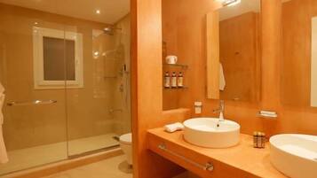 A modern bathroom with a glass shower enclosure, a large mirror, two sinks, and a vanity with storage.