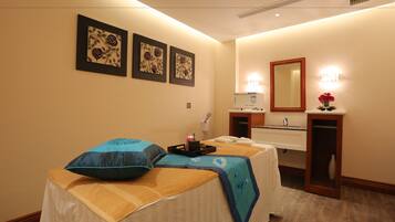 Ein Hotelzimmer mit Massagetisch, Schreibtisch mit Computer, Spiegel und Bildern an der Wand.