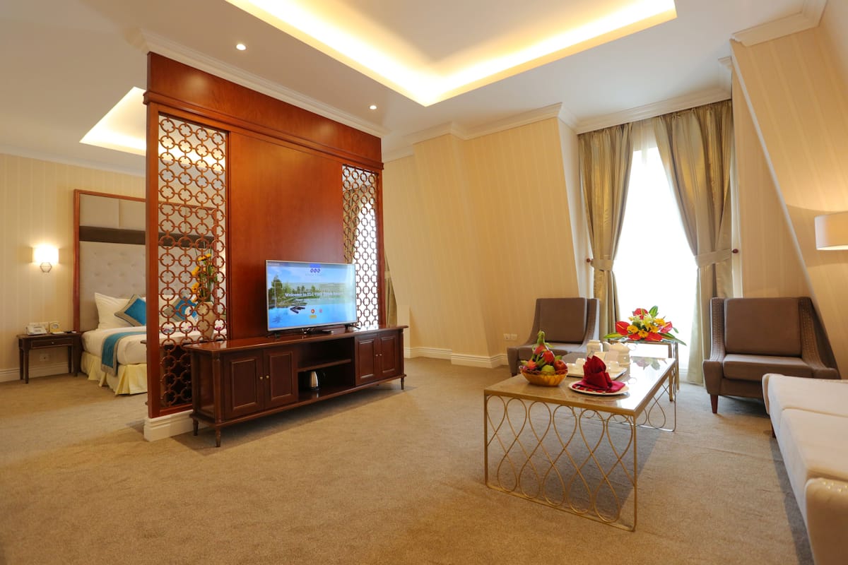 Ein Hotelzimmer mit Fernseher, einer Sitzecke und einem Esstisch mit Blumenarrangement.