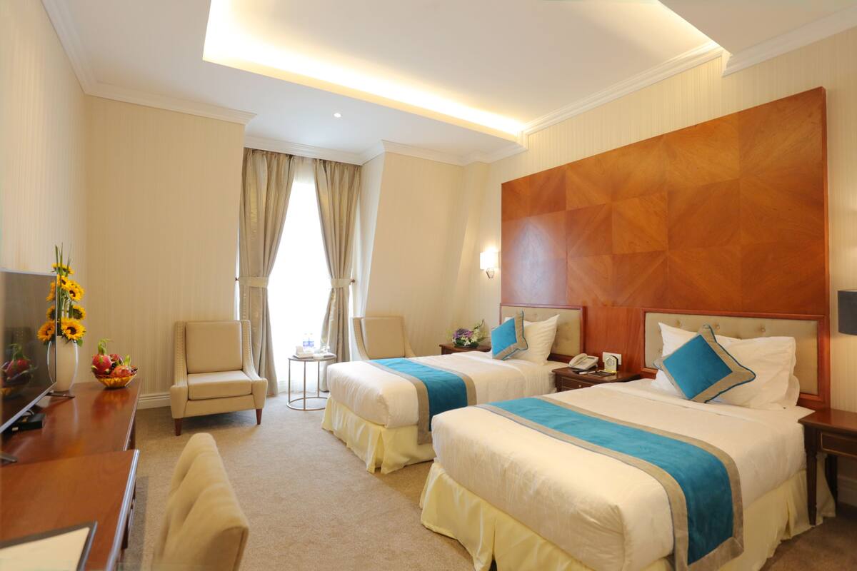 A hotel room with two beds, a desk, a chair, and a TV.