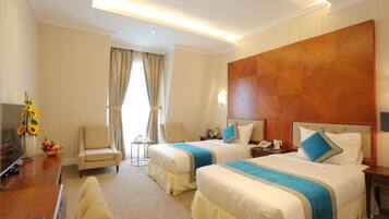 A hotel room with two beds, a desk, a chair, and a TV.