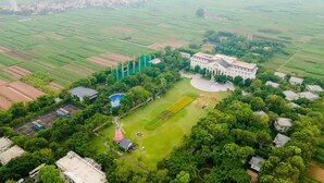 An aerial view of a large estate with a central building, expansive green fields, and a swimming pool. - FLC Luxury Resort Vinh Phuc (Vinh Phu)