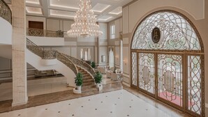A grand interior with a marble staircase, a large chandelier, and a decorative arched window. - FLC Luxury Resort Vinh Phuc (Vinh Phu)