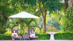 Two lounge chairs by a pool with a white umbrella, surrounded by lush greenery. - FLC Luxury Resort Vinh Phuc (Vinh Phu)