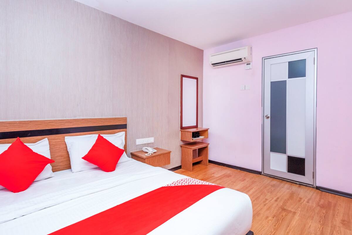 A hotel room with a bed, a bedside table, a mirror, an air conditioning unit, and a door.