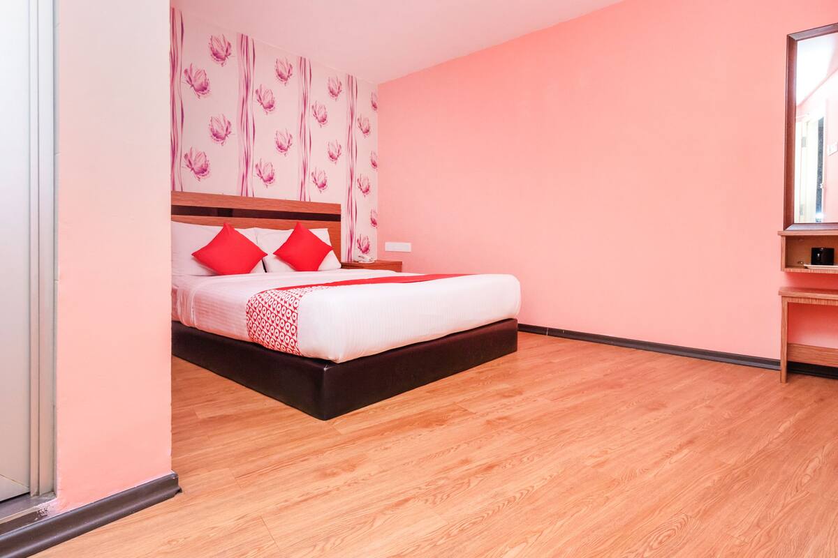 A bedroom with a bed, pink walls, and a wooden floor.