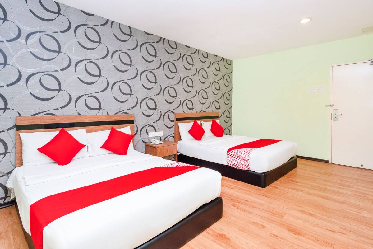 A hotel room with two beds, each with white bedding and red accents, a patterned wall, and a wooden floor.
