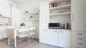 A modern kitchen with white cabinetry, a dining area with a table and chairs, and a microwave on the countertop. - Italianway Comfort - Bligny 19 A (Milan)