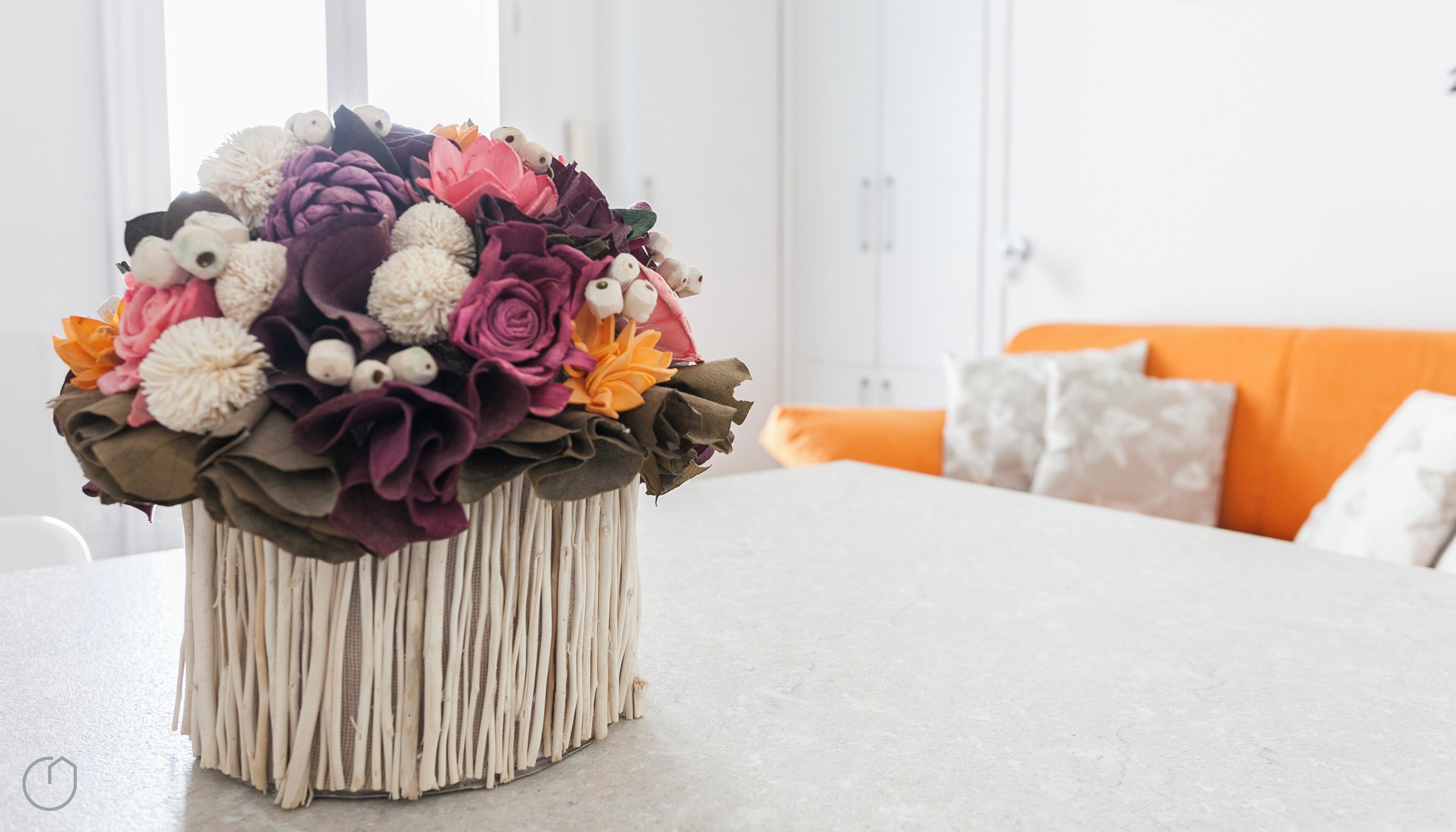 A vase with a floral arrangement on a table in a room with a white wall and an orange couch.