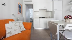A modern kitchen with white cabinets, a dining area with a white table and chairs, and a living area with an orange sofa and butterfly-patterned pillows. - Italianway Comfort - Bligny 19 A (Milan)