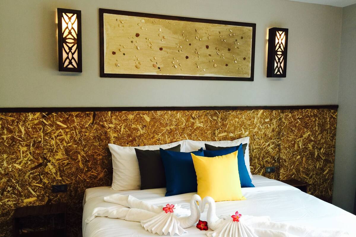 A hotel room with a bed, decorative pillows, wall art, and a headboard with a wood-like texture.