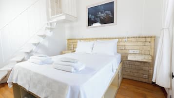 Una habitación de hotel con una cama, ropa de cama blanca, cabecero de madera, una escalera y un cuadro en la pared.