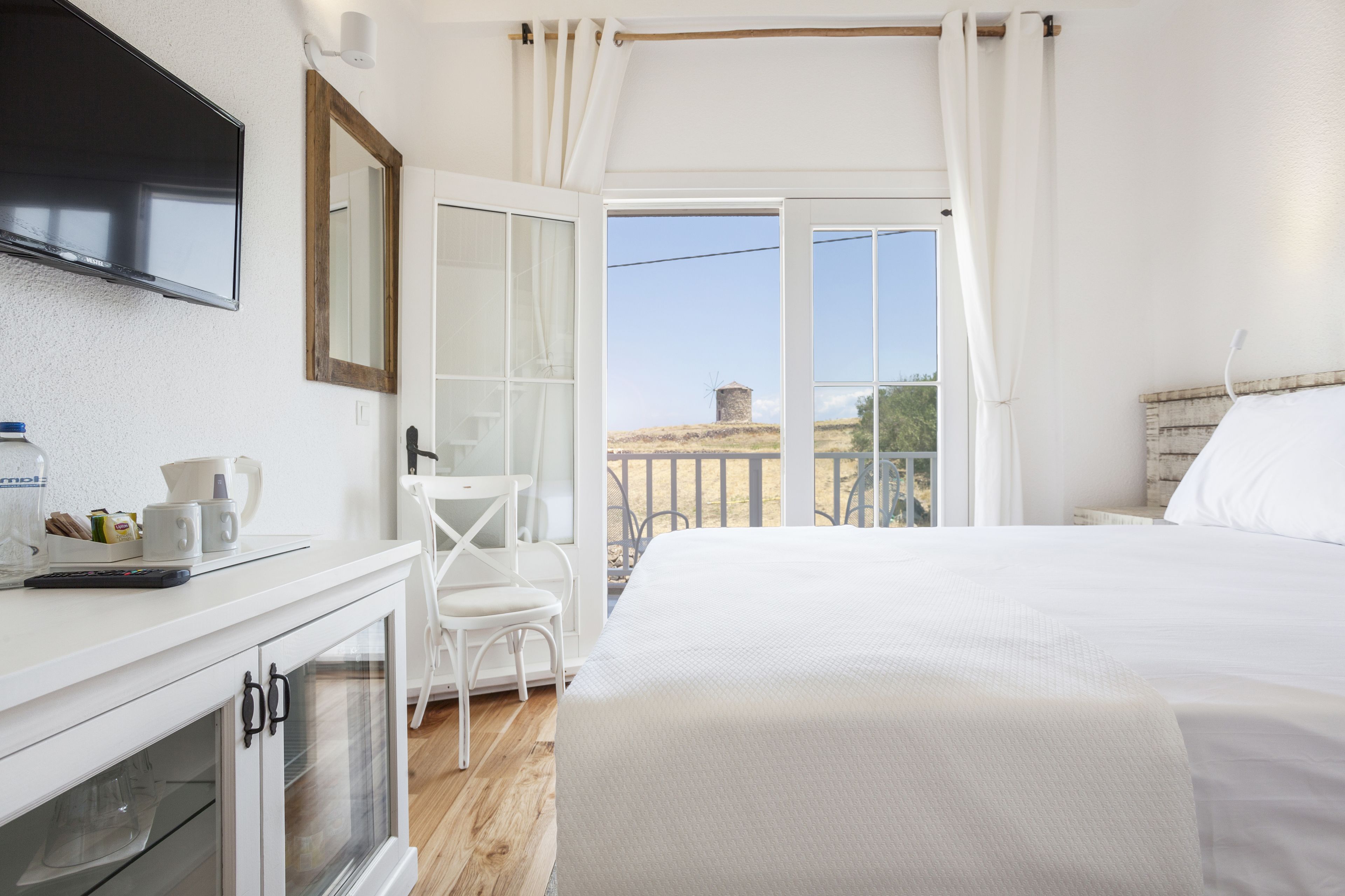 Un dormitorio con cama, escritorio, silla, televisor y balcón con vistas al campo.