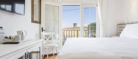 Un dormitorio con cama, escritorio, silla, televisor y balcón con vistas al campo.