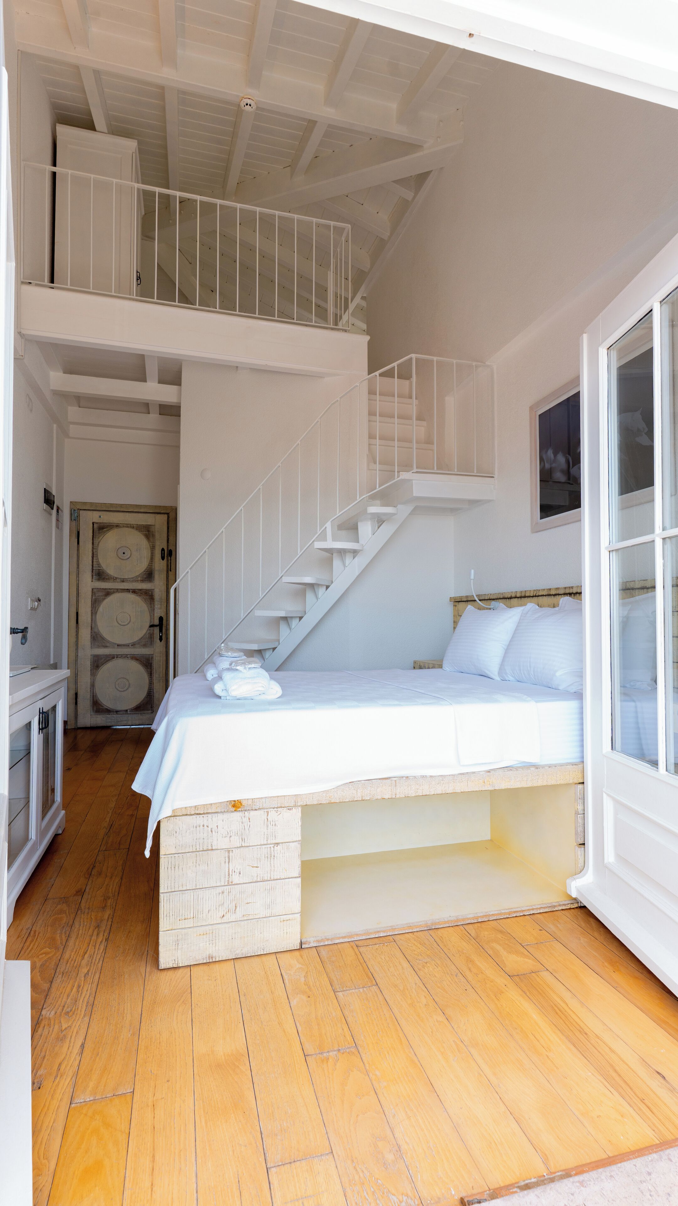 A bedroom with a lofted sleeping area, a staircase, and a large window.