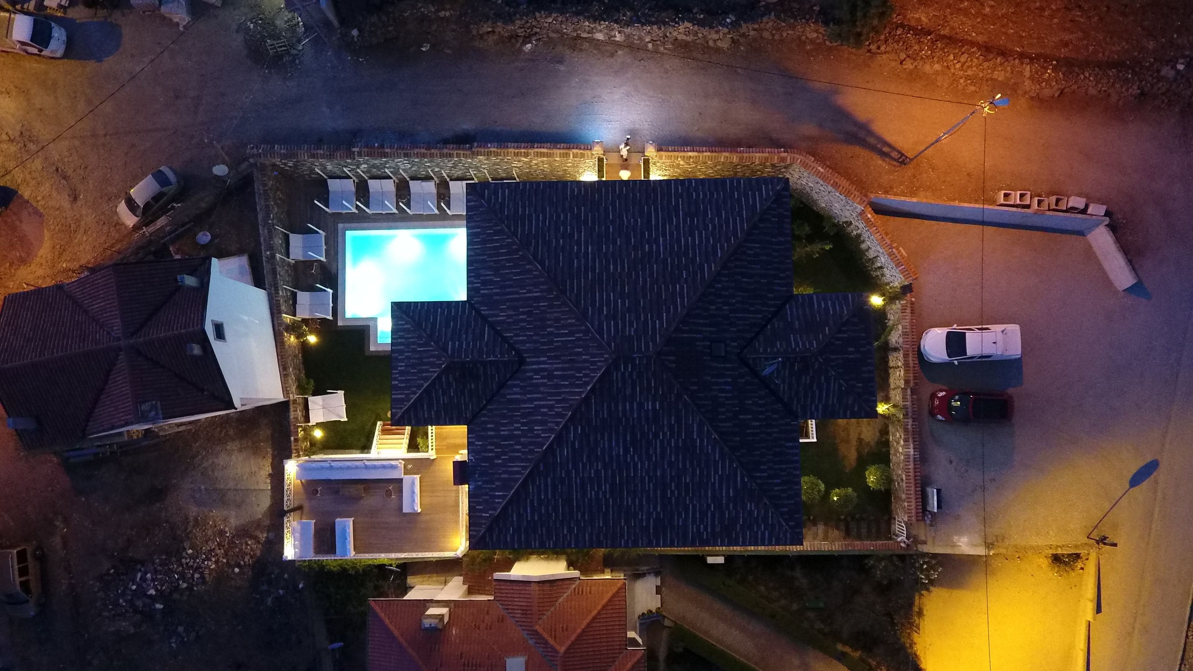 An aerial view of a residential area with a swimming pool, multiple houses, and parked cars.