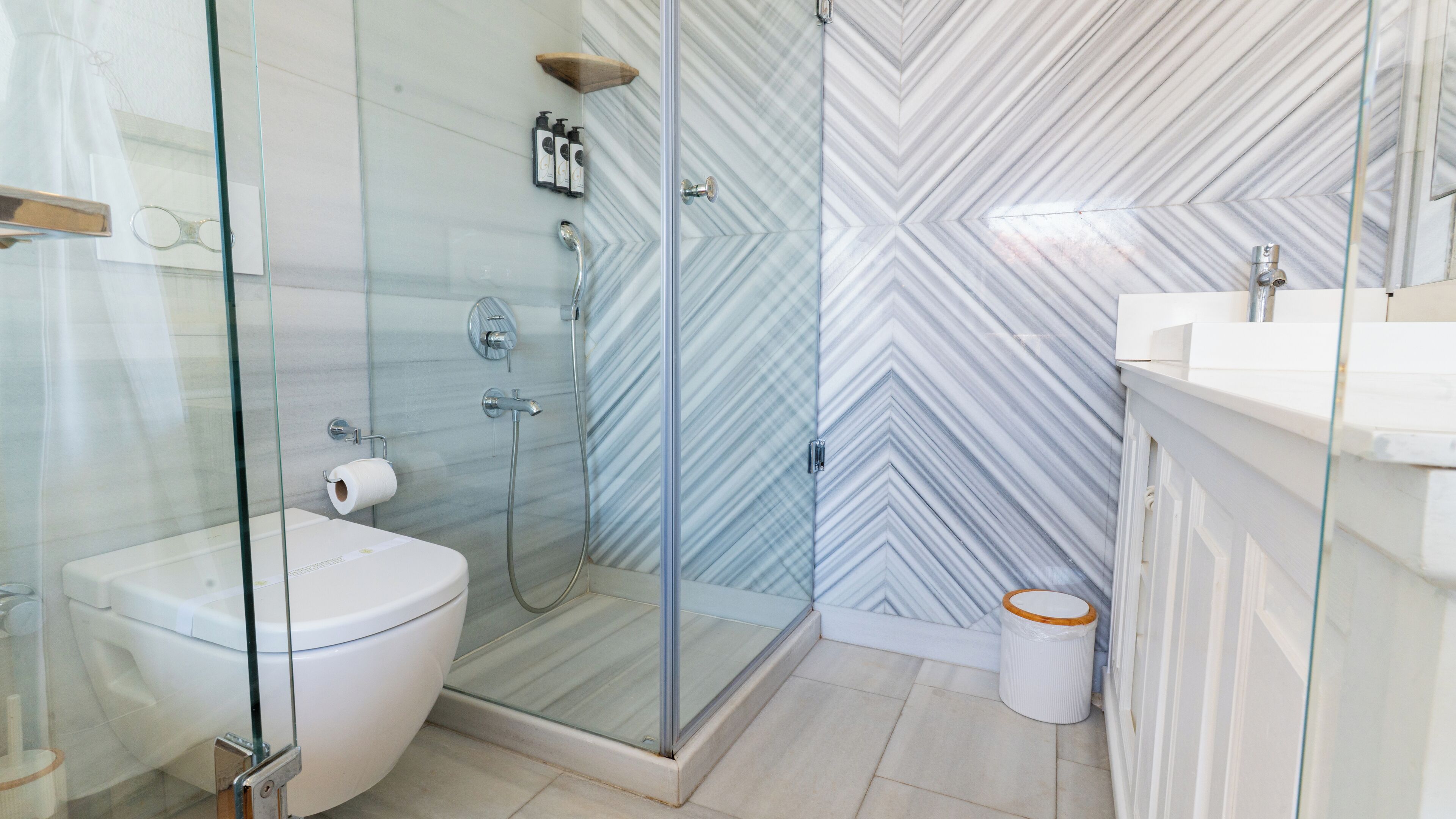 Un baño moderno con cabina de ducha de vidrio, inodoro y lavamanos con espejo.