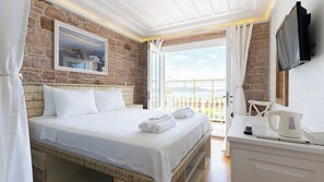 A hotel room with a bed, a desk with a kettle, a TV, and a balcony with a view. - Cunda Piano Otel (Ayvalik)
