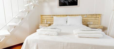 A neatly made bed with white linens and towels, a wooden headboard, and a white staircase to the left.