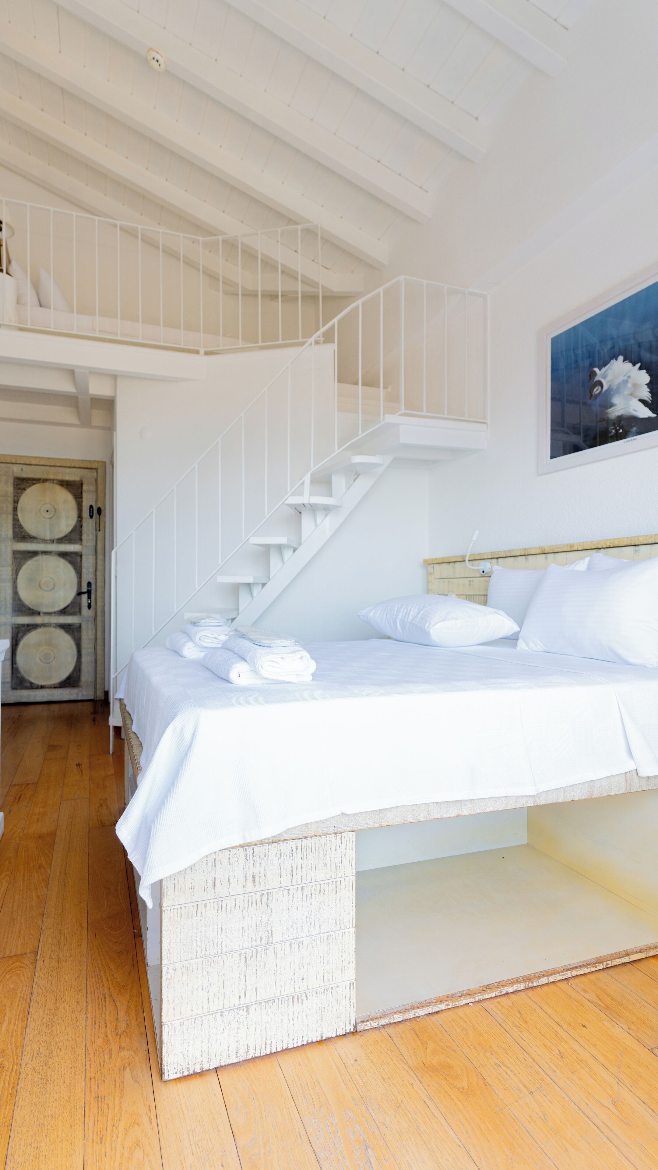 A bedroom with a large bed, a wooden floor, a white staircase, and a door with circular patterns.