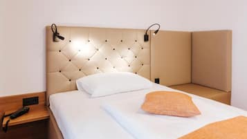 Habitación de hotel con un cabecero capitonado, una cama individual con ropa blanca, un cojín naranja y una mesita de noche con lámpara.