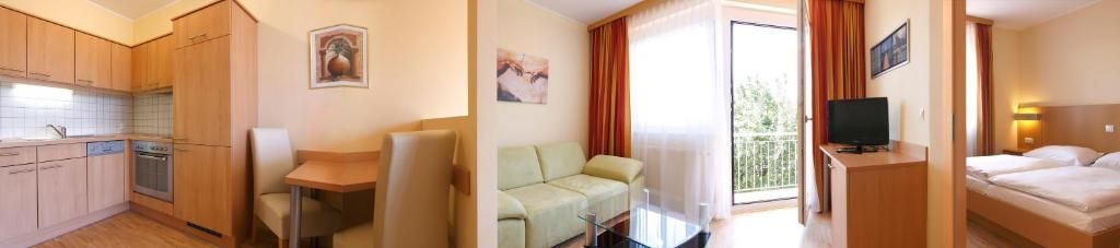 Habitación de hotel con kitchenette, sofá, televisor y balcón con cortinas.