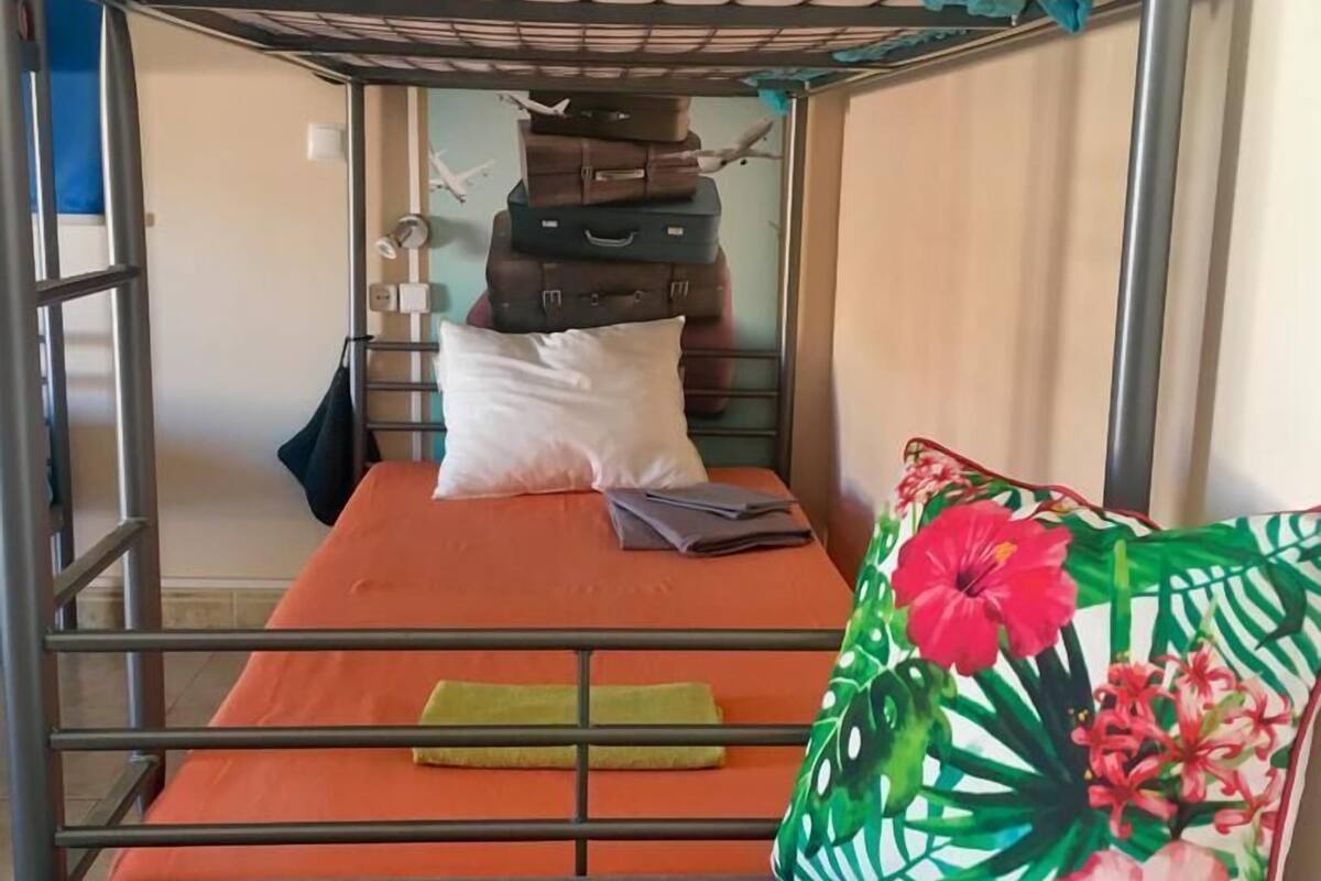 Un lit superposé avec une barre supérieure verte, un lit simple en dessous et un oreiller à motifs floraux.