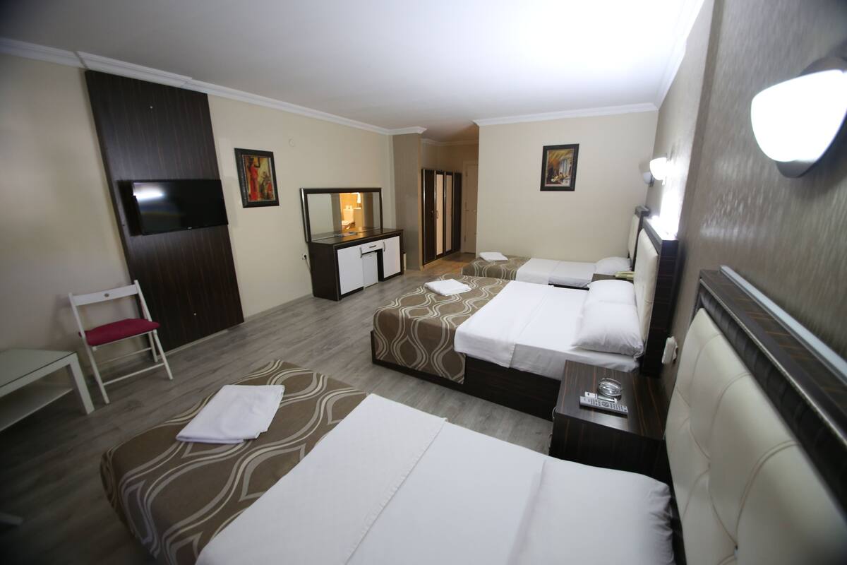 A hotel room with three beds, a desk, a TV, and a wardrobe.
