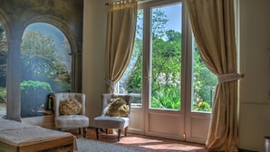 A room with a large arched doorway, a cushioned chair, a wooden bench, and a view of greenery through a glass door. - Verdmont (Acqui Terme)