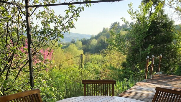 A wooden table with a bottle of wine and a glass, surrounded by chairs, set outdoors with a view of a lush landscape. - Verdmont (Acqui Terme)