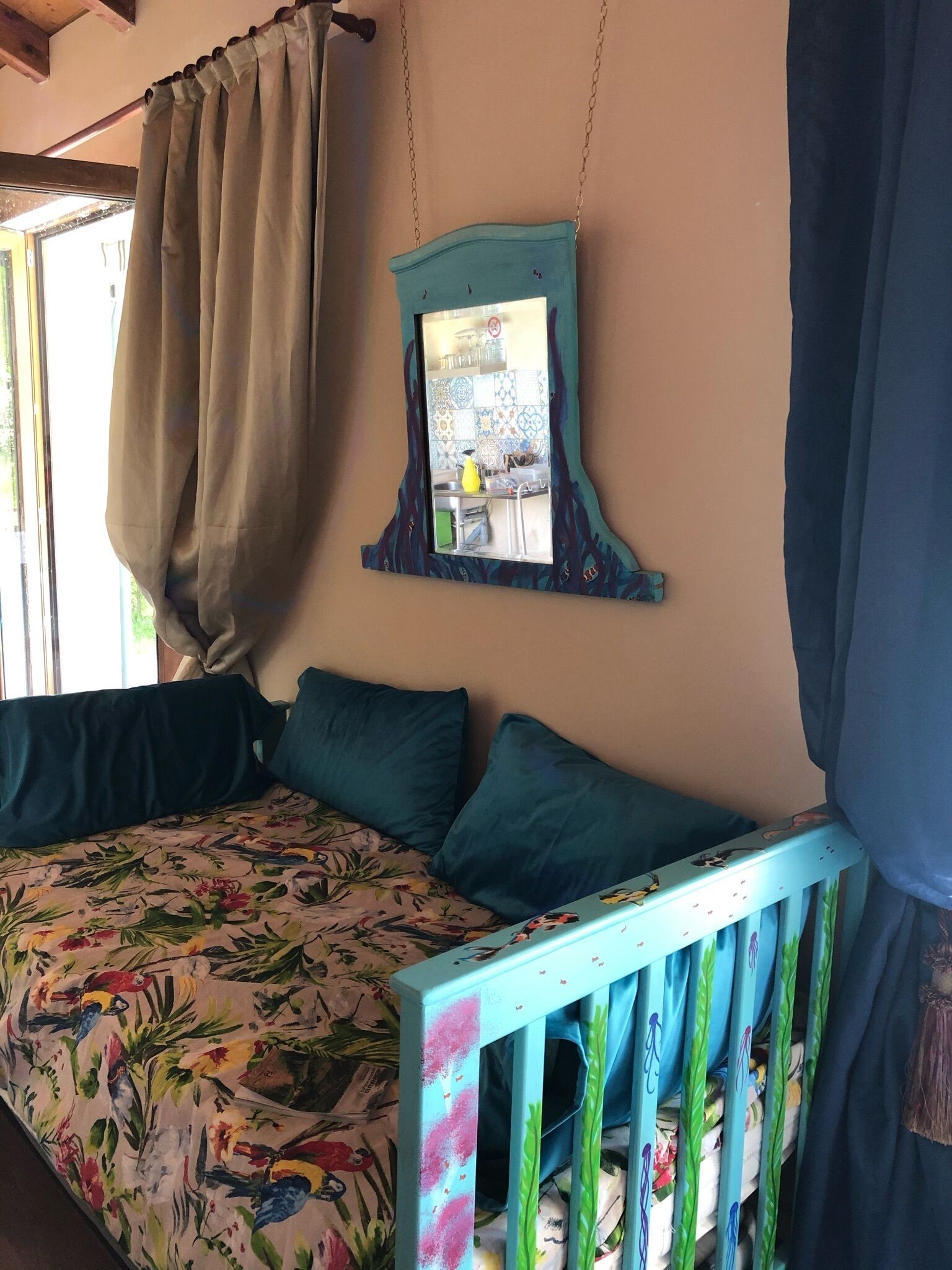 Un lit avec une literie à motifs floraux, un miroir suspendu et un berceau avec un cadre bleu.