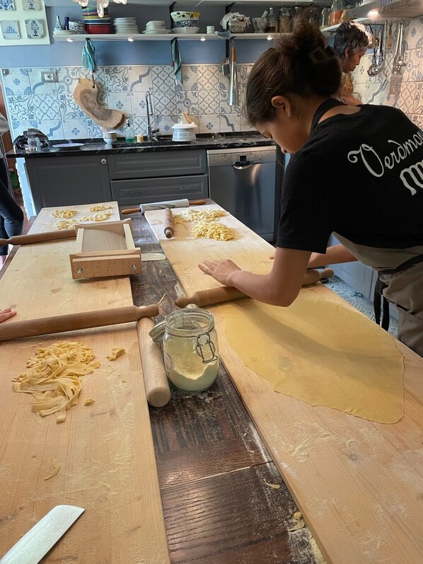 A kitchen with a wooden countertop, rolling pins, a rolling pin stand, a jar of flour, and pasta sheets.