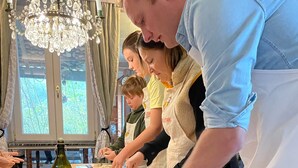A group of people in a kitchen preparing food, with a wooden table, rolling pin, and a bottle of olive oil visible. - Verdmont (Acqui Terme)