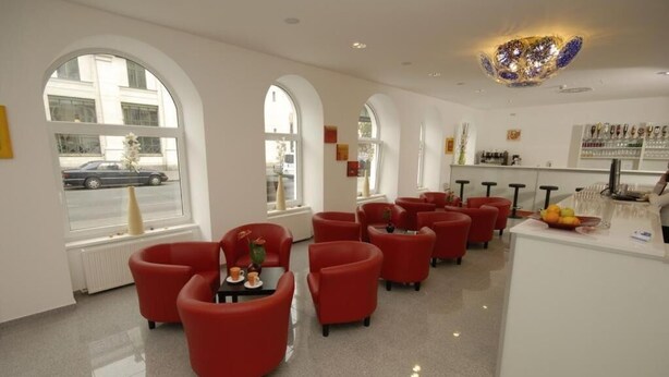 A modern hotel lobby with red chairs, a reception desk, and large arched windows. - Hotel City Residence (Vienna)