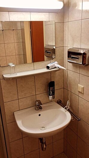 A bathroom with a sink, mirror, towel dispenser, and a hand dryer. - Hotel City Residence (Vienna)