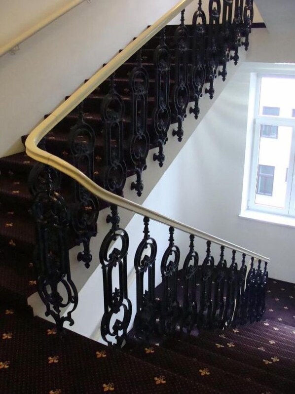 Una escalera con barandillas de metal negro ornamentado y un pasamanos blanco.