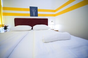 Habitación de hotel con una cama grande, dos almohadas, cabecera roja, lámpara de noche y una obra de arte en la pared.