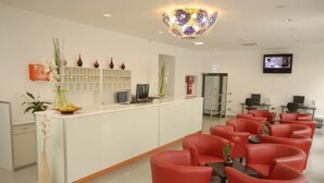 A reception area with a white counter, red chairs, a television, and decorative vases. - Hotel City Residence (Vienna)