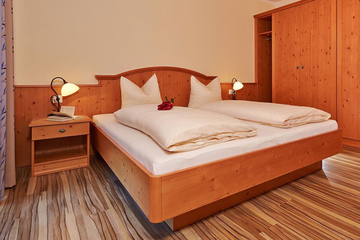 Un lit en bois, avec deux tables de chevet, chacune équipée d’une lampe, dans une pièce dont le sol et les murs sont recouverts de bois.