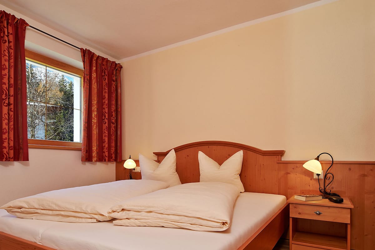 Un lit bien fait, avec du linge de lit blanc, une tête de lit en bois et deux lampes de chevet.