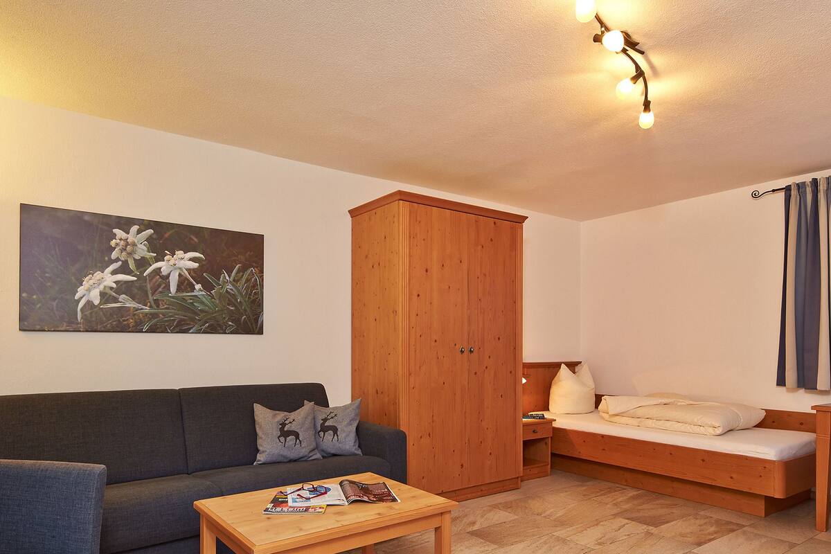 Un salon chaleureux avec un canapé, un meuble en bois, une petite table avec des magazines et un lit avec une table de chevet.