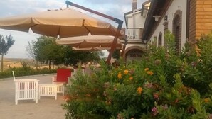 A building with a covered outdoor seating area, a brick wall, and a garden with yellow flowers. - Relais I Dolci Grappoli (Larino)