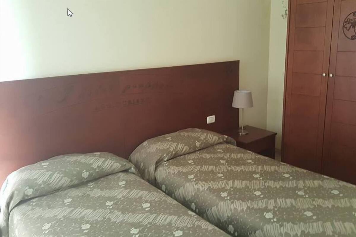 A room with two beds, a nightstand with a lamp, and a wooden wardrobe.