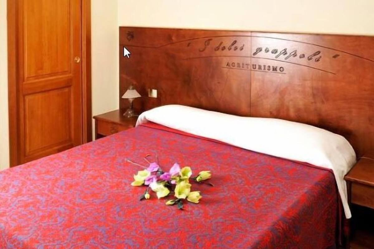A room with a wooden bed, a nightstand, a wall-mounted lamp, and a door.