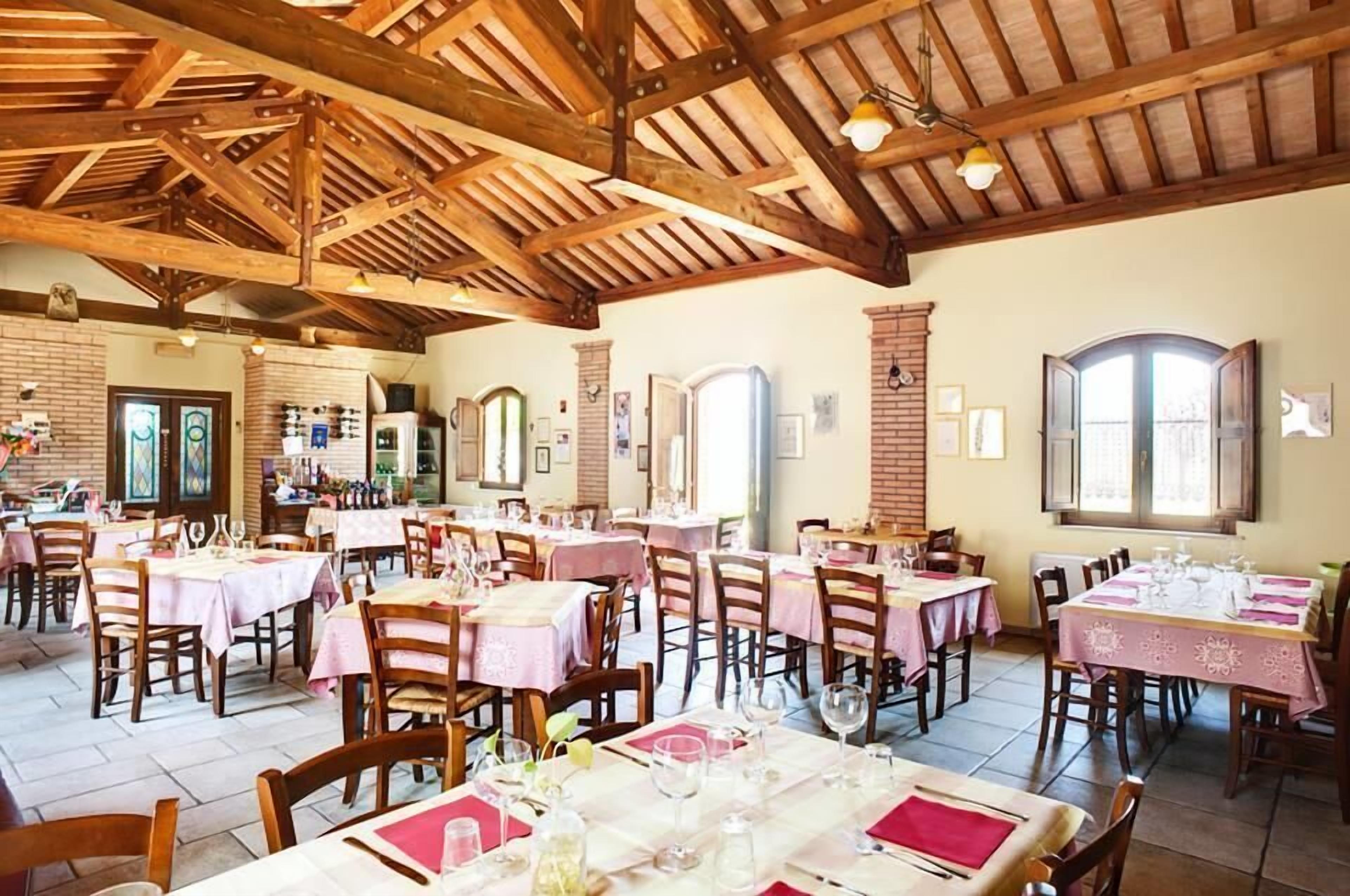 A restaurant with wooden beams, tables set with pink tablecloths, and a brick wall.