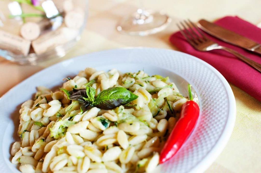 A plate of pasta with a red chili pepper and a basil leaf on the side.