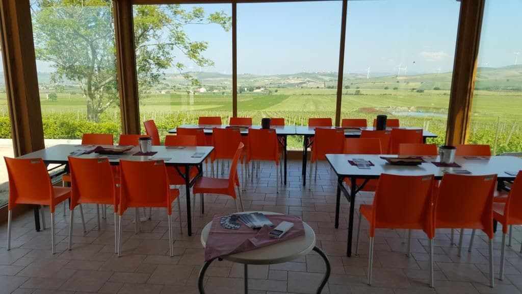 A dining area with tables and chairs, large windows with a view of fields and wind turbines.