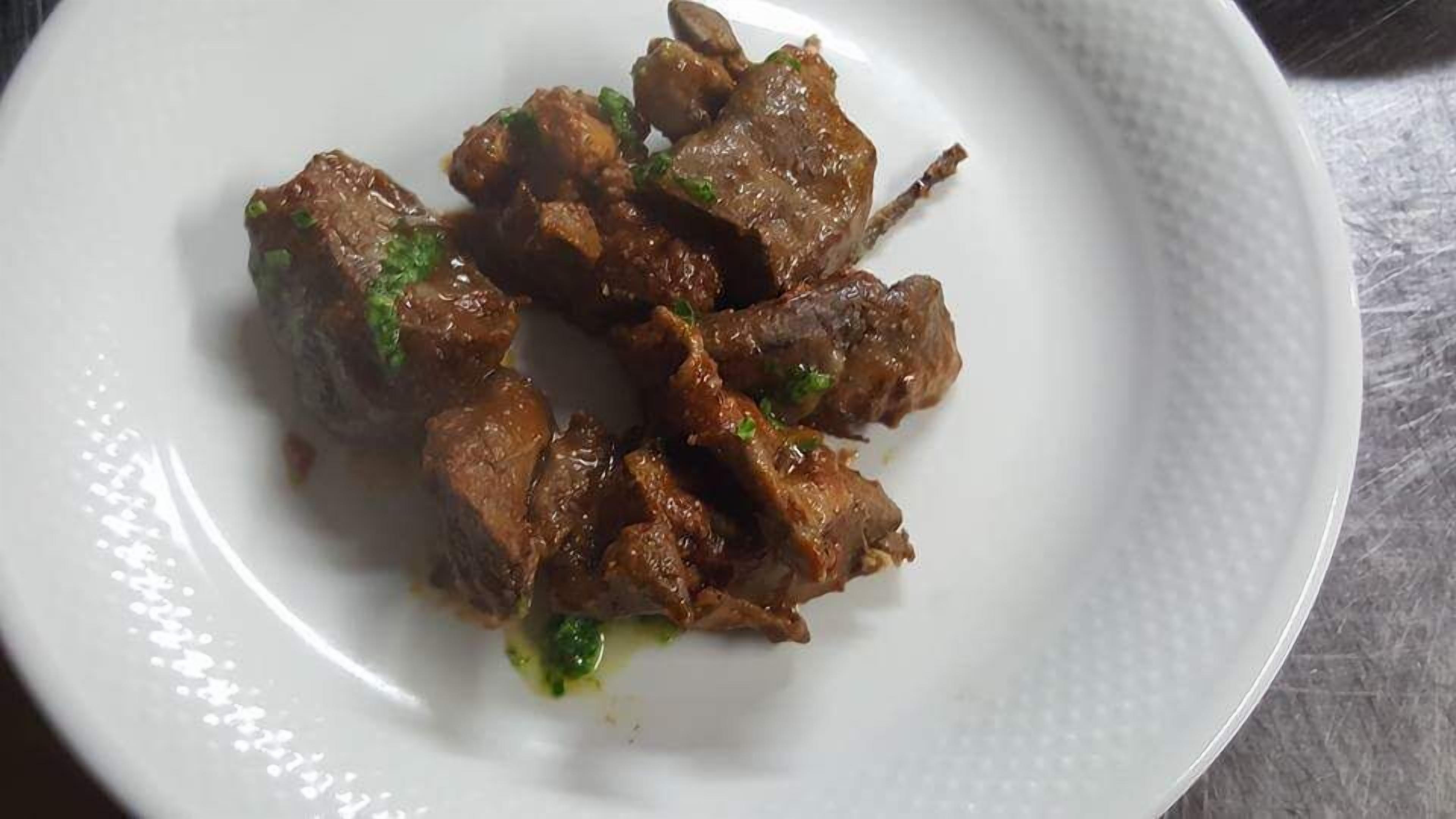 Une assiette blanche contenant un plat de viande, agrémenté d’herbes vertes.
